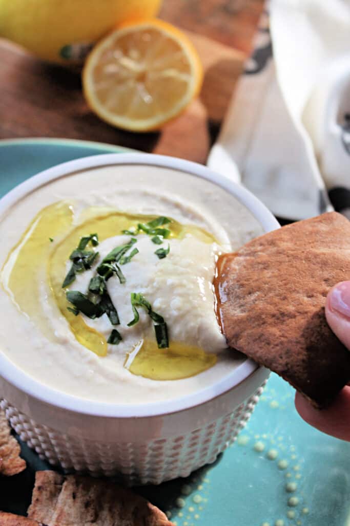 Hand dipping a pita chip into White Bean Dip.