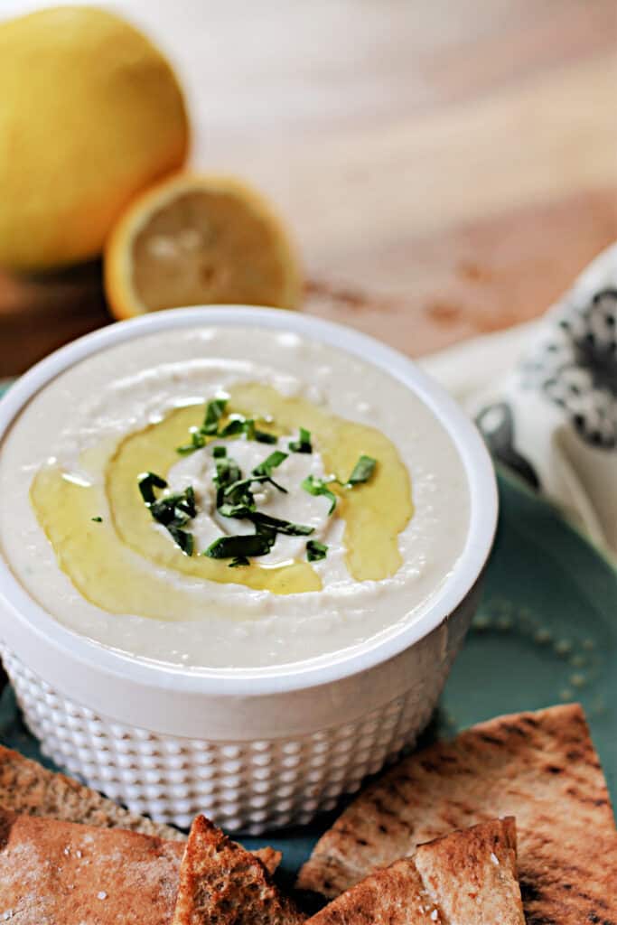 White Bean Dip in a white ramekin with olive oil and herbs on top.