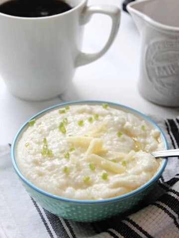 Bowl of cheese grits topped with shredded cheddar cheese and chives.