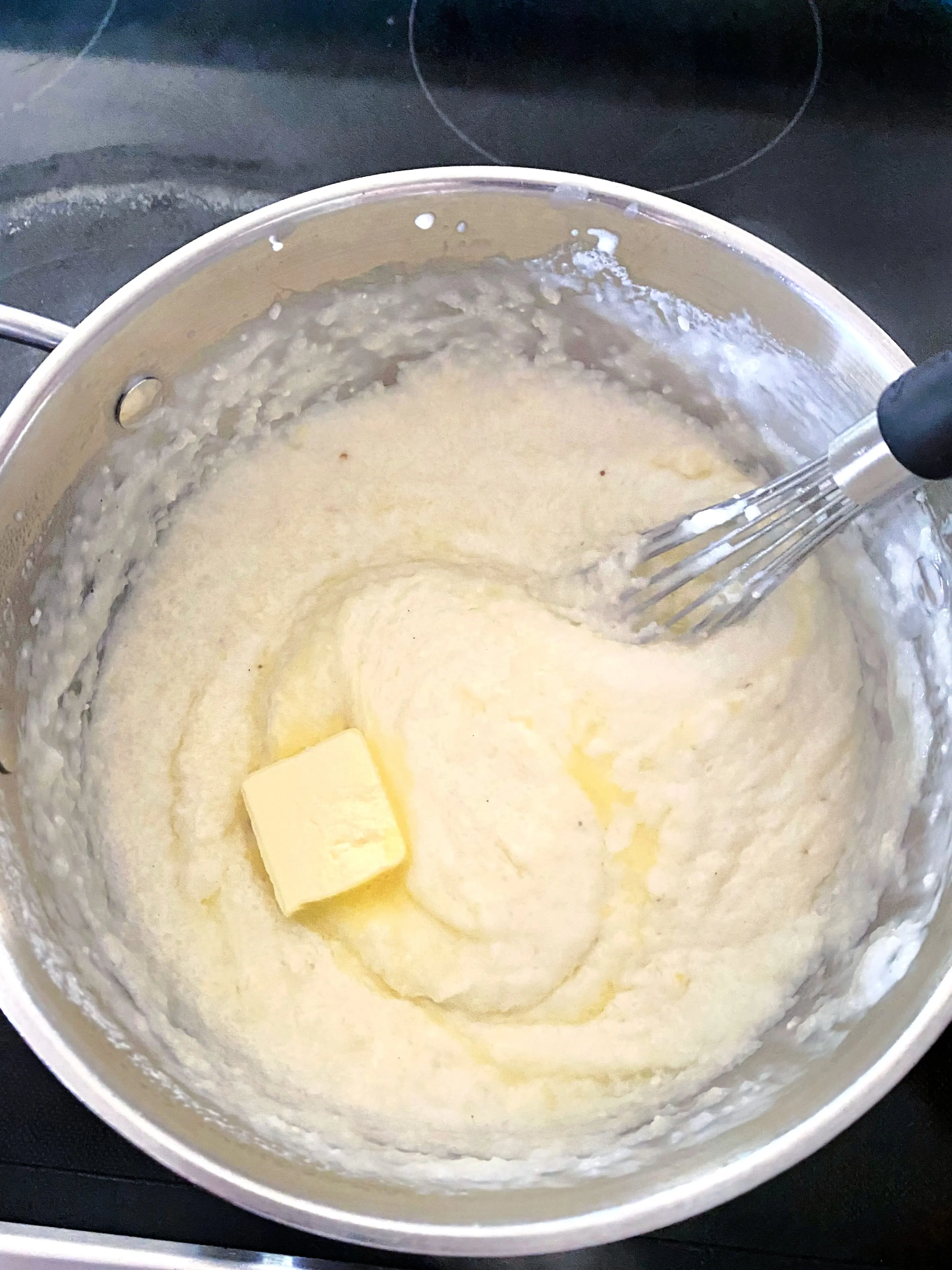 Finished cheese grits in pot after whisking with added pat of butter.