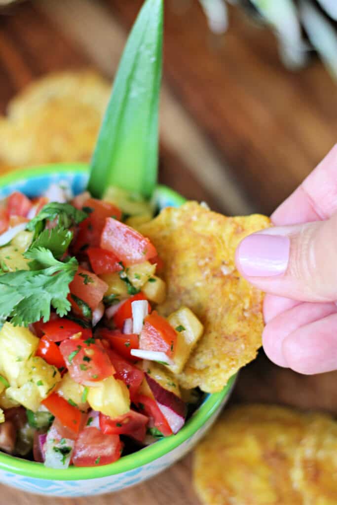 Hand dipping a plantain chip into a bowl of Pineapple Pico de Gallo.