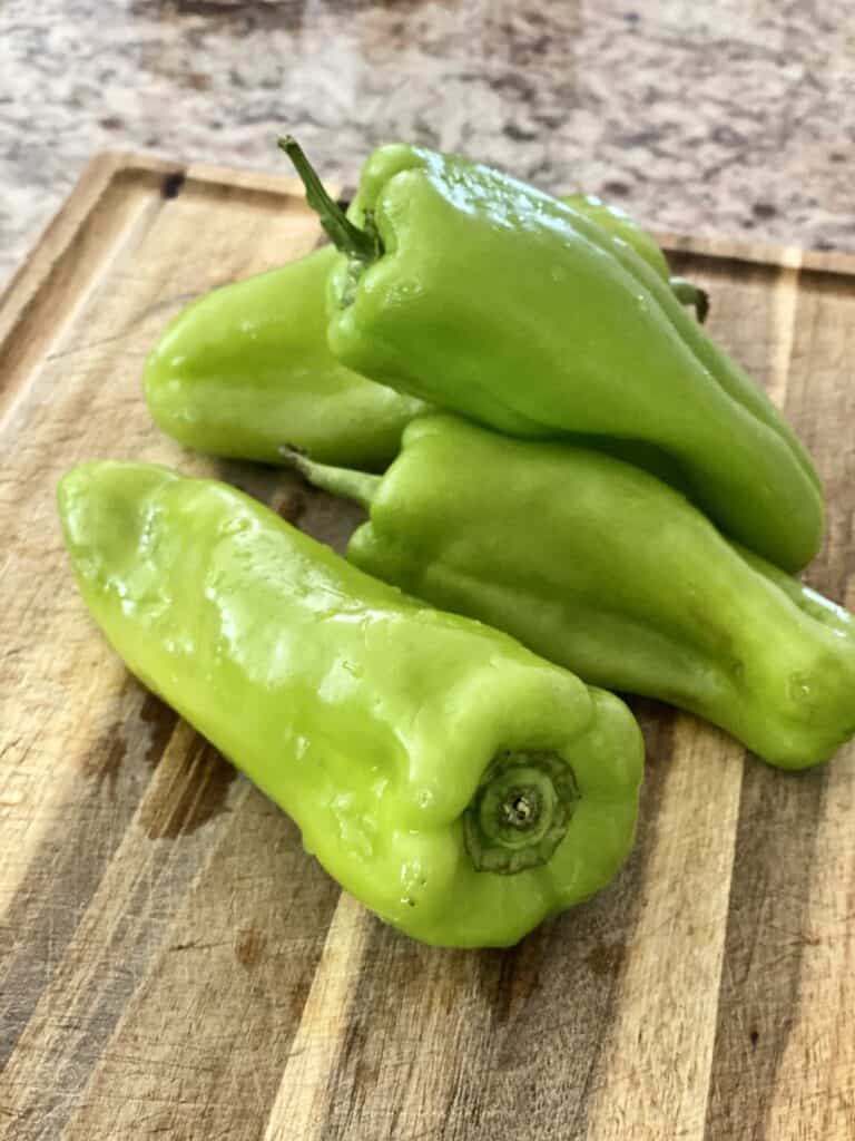 Whole Cubanelle peppers on a wooden cutting board.