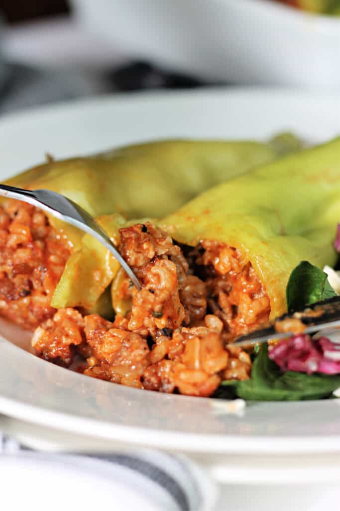 Fork and knife cutting into a stuffed cubanelle pepper.