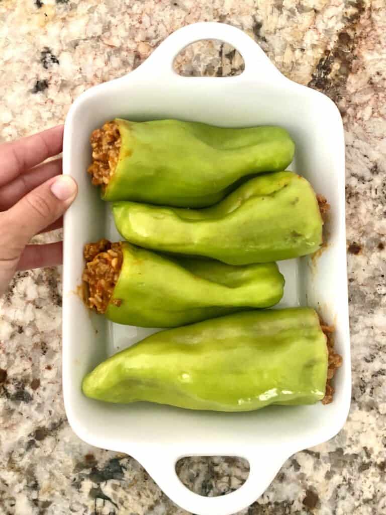 Four Stuffed Cubanelle Peppers in a white baking dish.