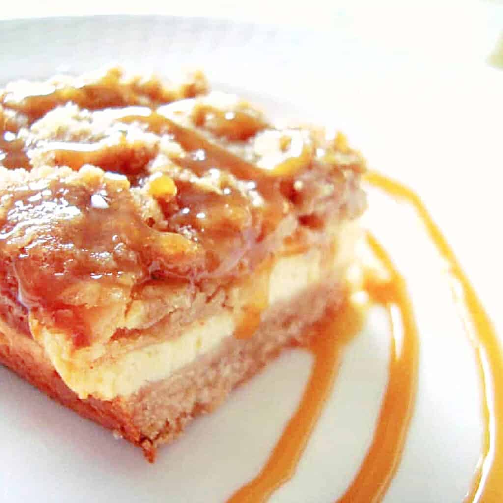 An apple crumble cheesecake bar on a white plate with a decorative caramel swirl.