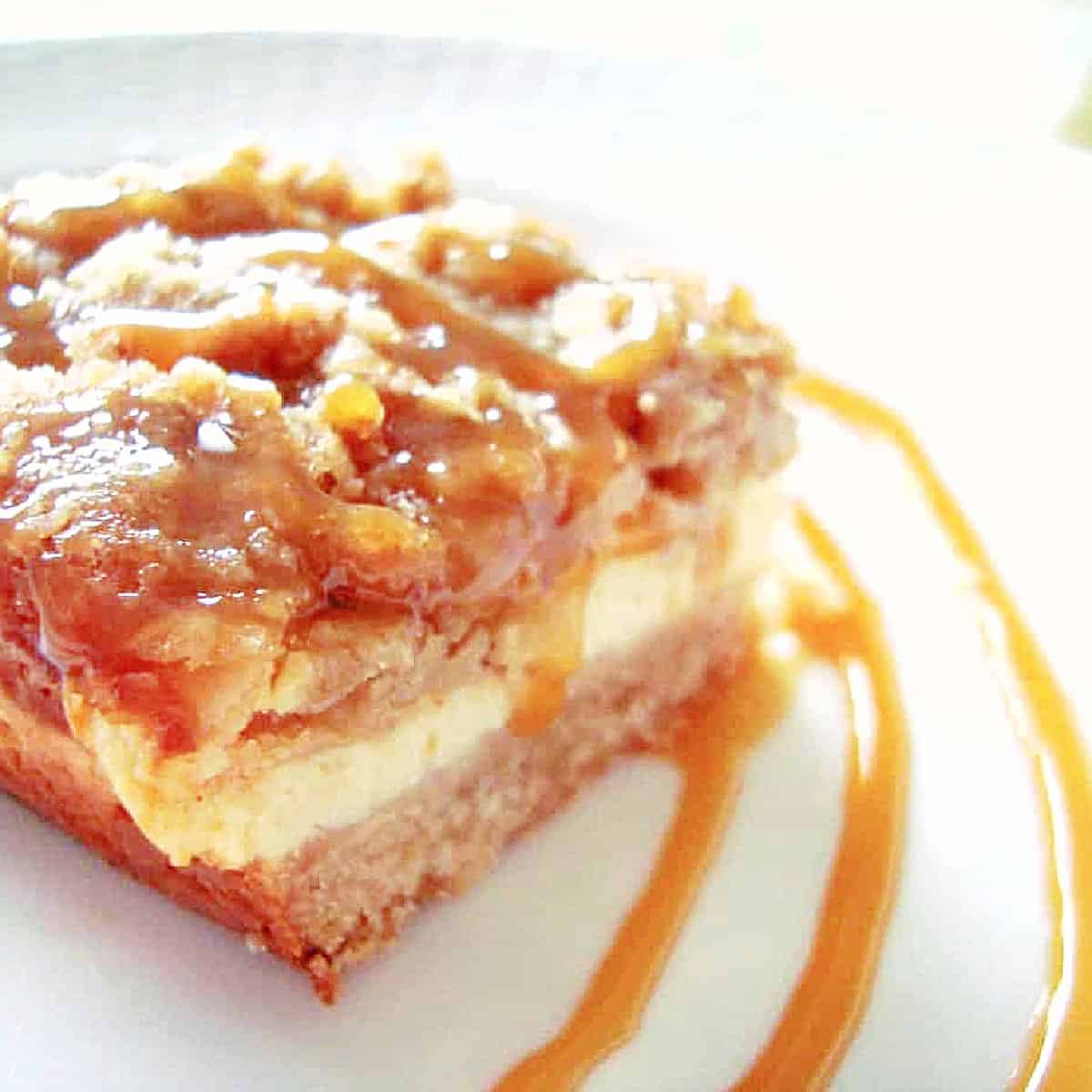 An apple crumble cheesecake bar on a white plate with a decorative caramel swirl.