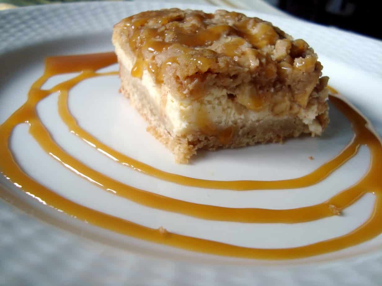 A side view of the layers of cheesecake and crust on apple crumble cheesecake bars on a plate with swirls of caramel.