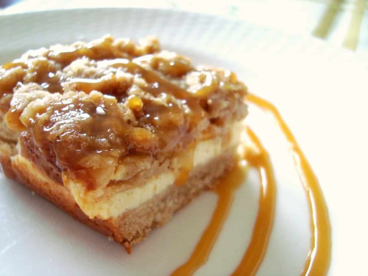 A close up of an apple crumble cheesecake bar on a white plate.