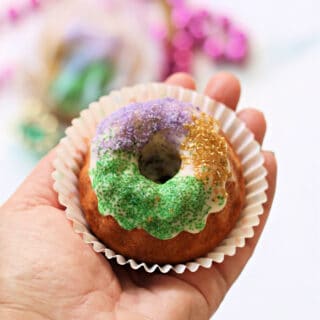 Hand holding a mini king cake in a cupcake liner.
