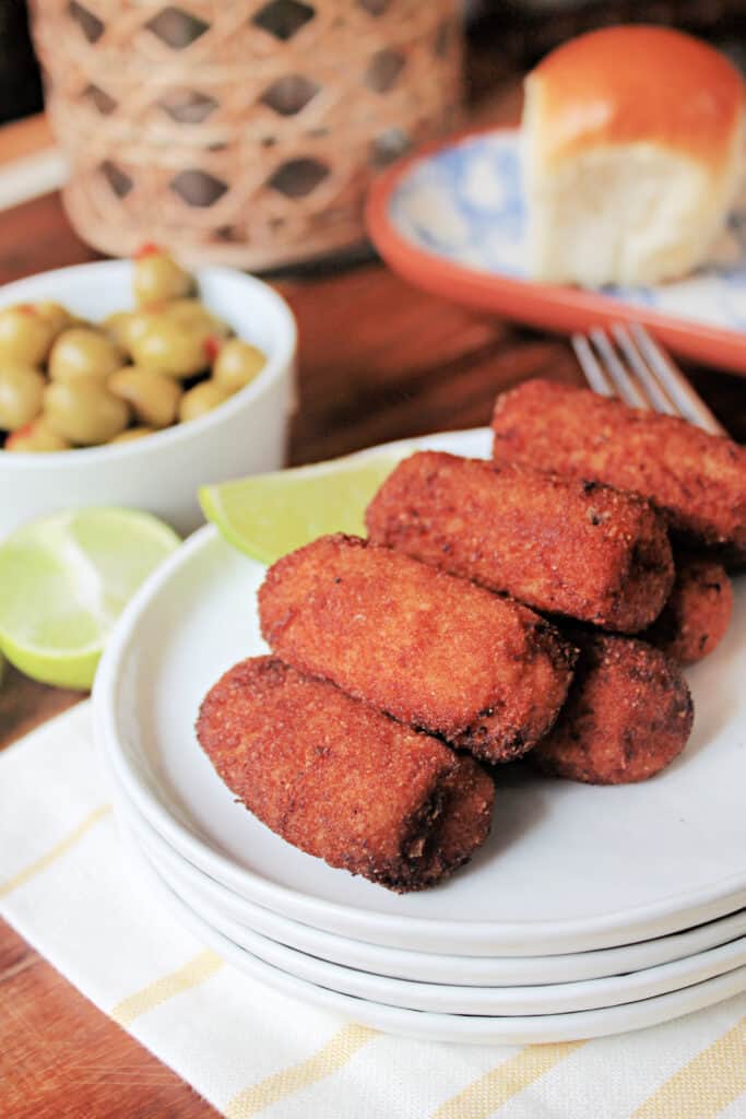 A white appetizer plate piled with a stack of Croquetas de Jamon.