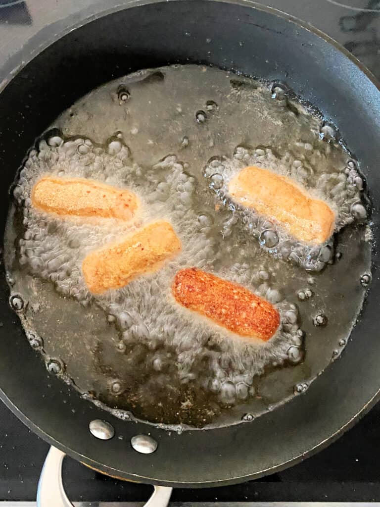 Croquetas de Jamon frying in oil in a skillet.