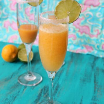 Two champagne glasses filled with Tropical Fruit Bellinis on a turquoise backdrop.