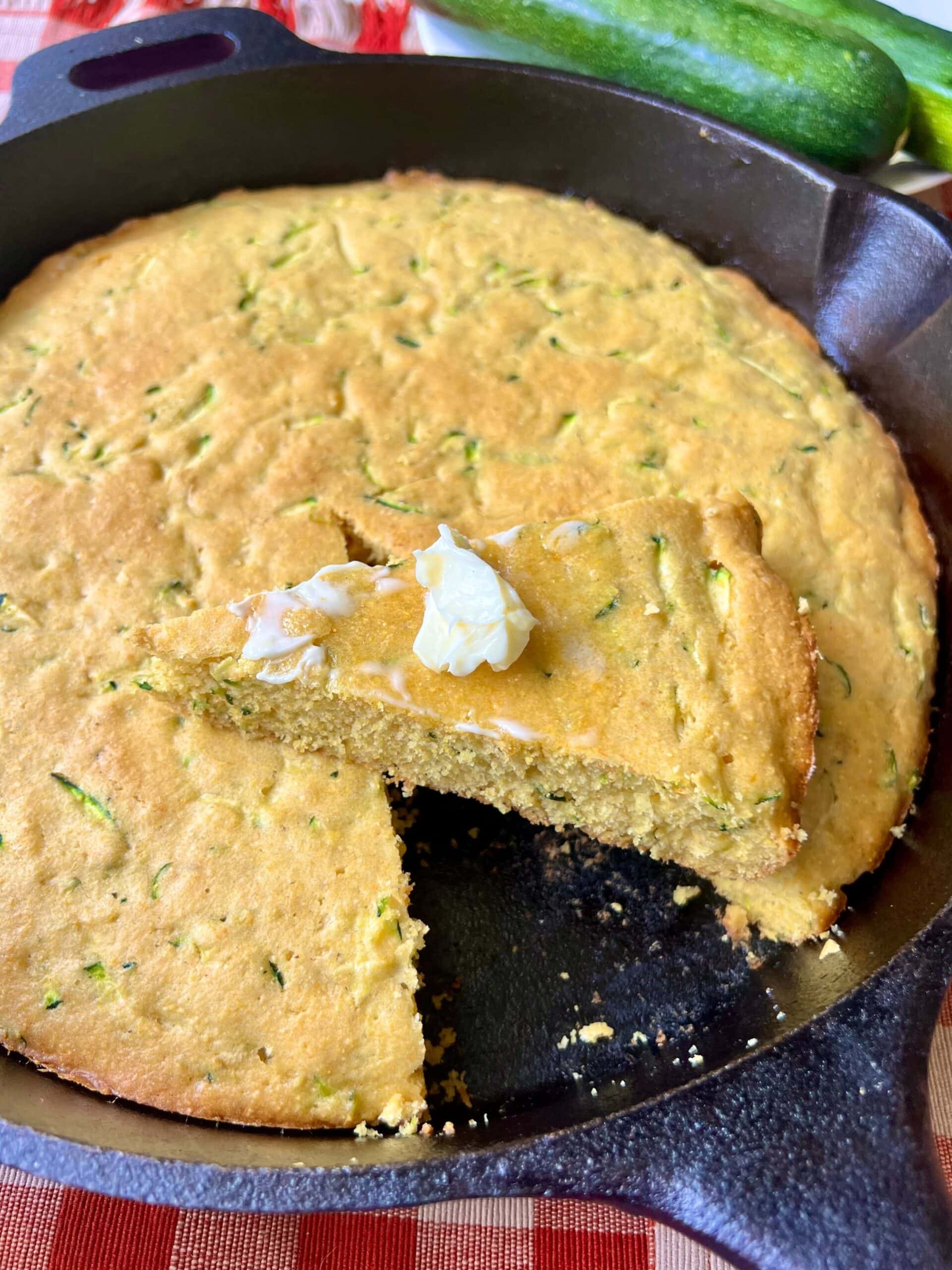 A wedge of zucchini cornbread topped with a pat of butter.