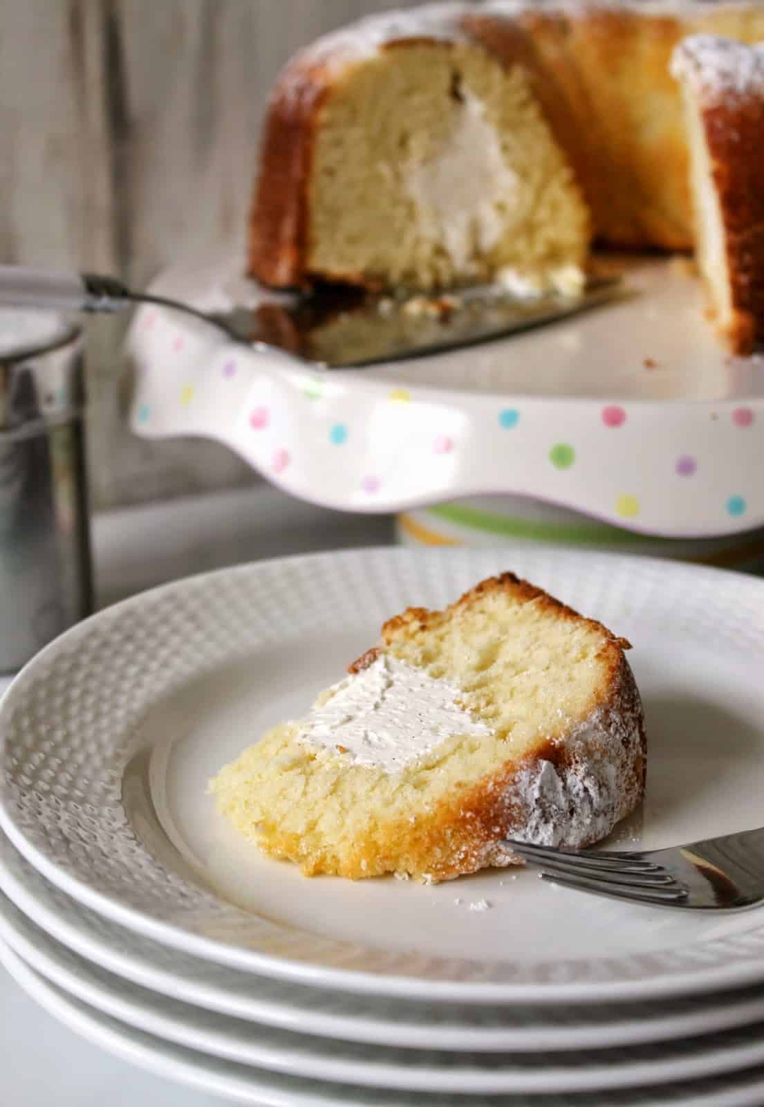 A slice of Twinkie Bundt Cake on a stack of white plates with a cake plate in the background.