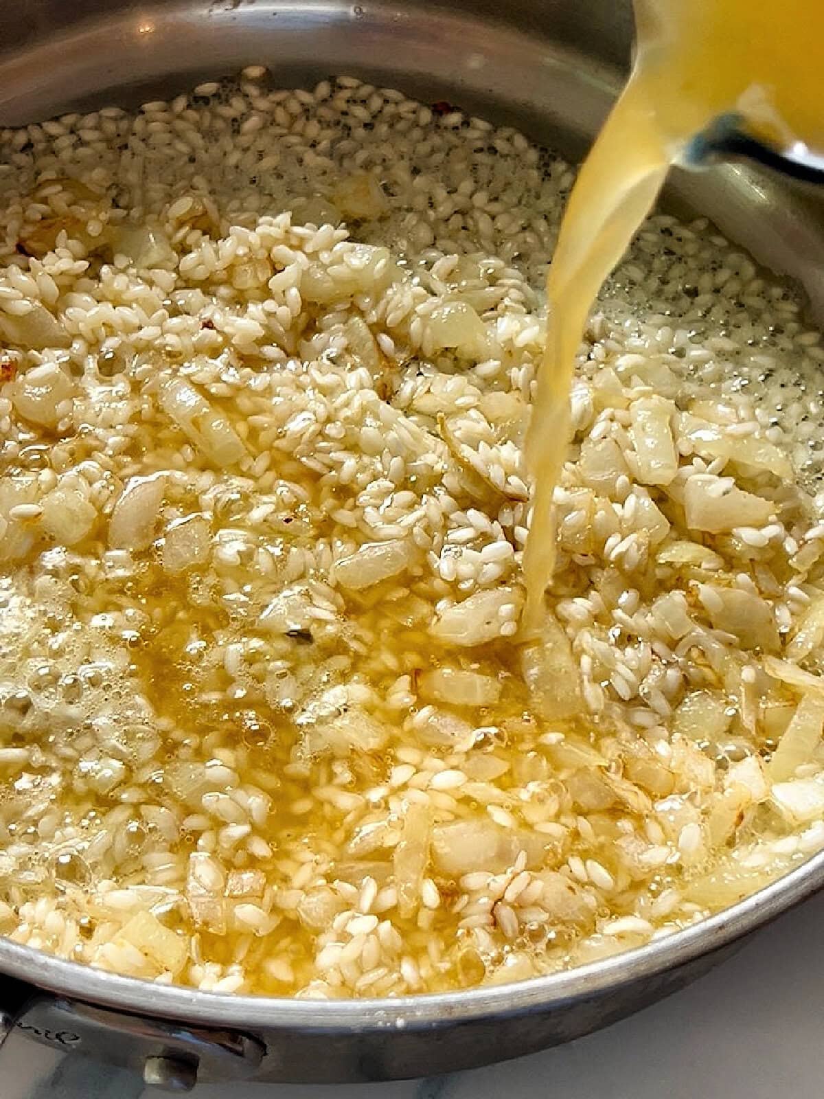Deglazing the pan of arborio rice and aromatics with vegetable broth.