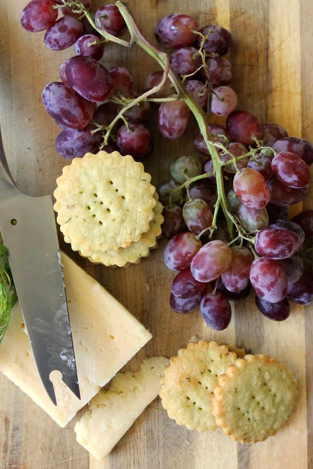 Cheese wafers, grapes and a block of cheese on a wooden board.