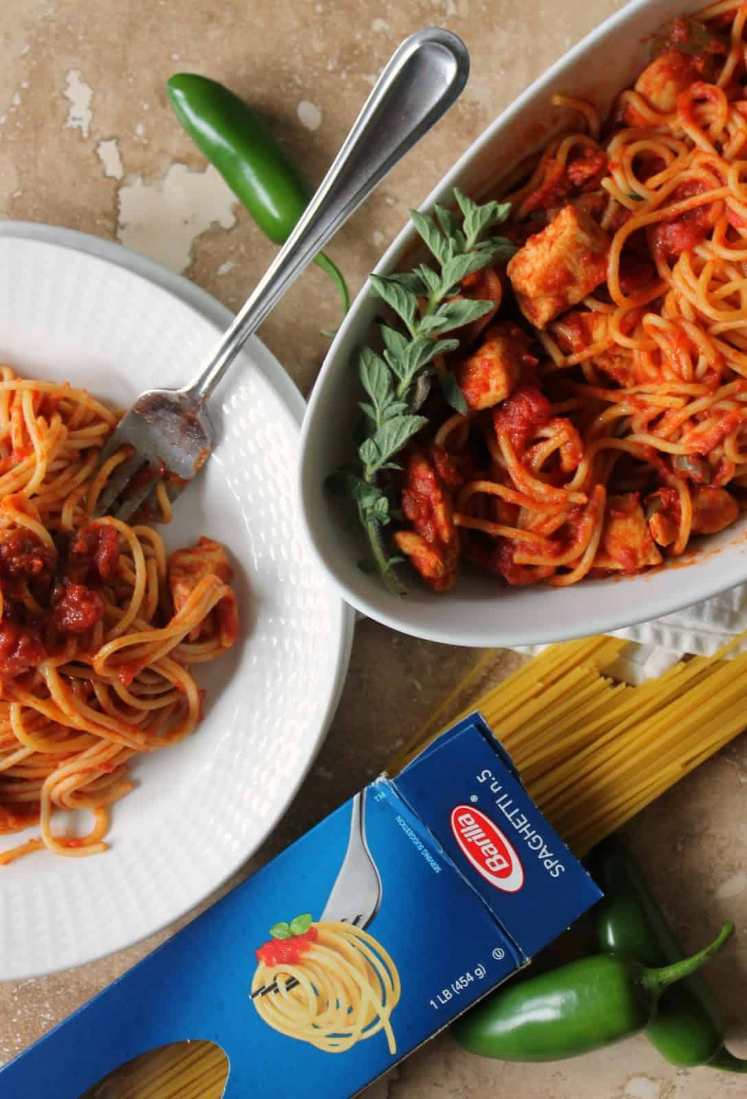 Overhead shot of Spaghetti with Chicken & Spicy Tomato Sauce on a dish and in serving dish with dry spaghetti noodles next to it.