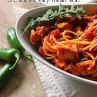 Close up of Spaghetti with Chicken & Spicy Tomato Sauce in an oval bowl with jalapeno peppers next to it.