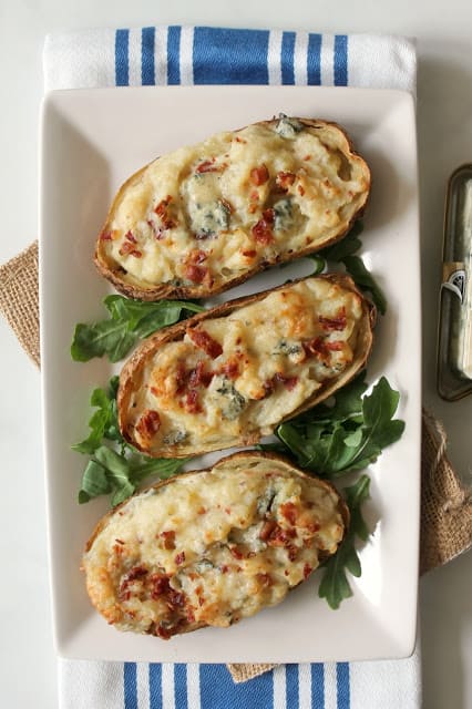 A white platter of 3 Blue Cheese & Bacon Twice Baked Potatoes with blue and white striped kitchen towel underneath.