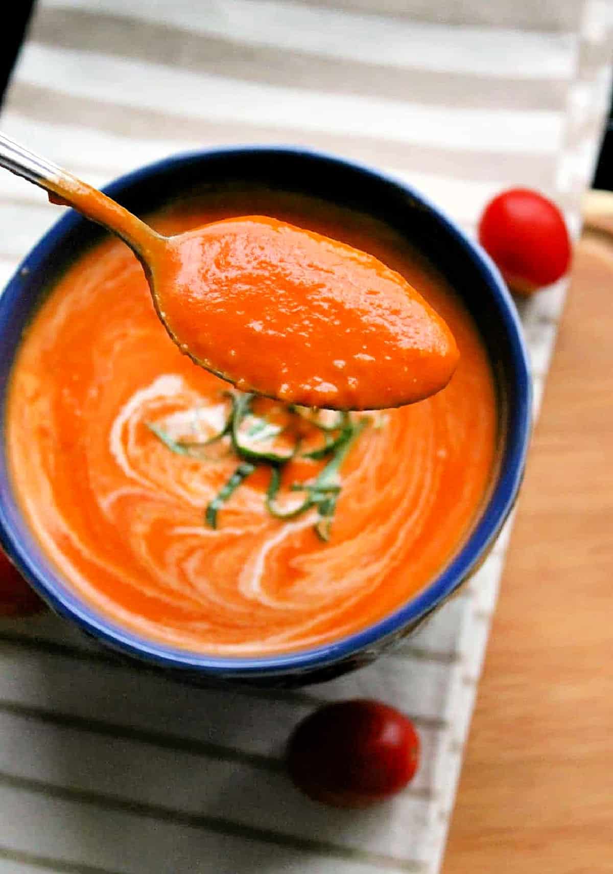 A spoonful of spicy tomato soup being held up over a bowl.
