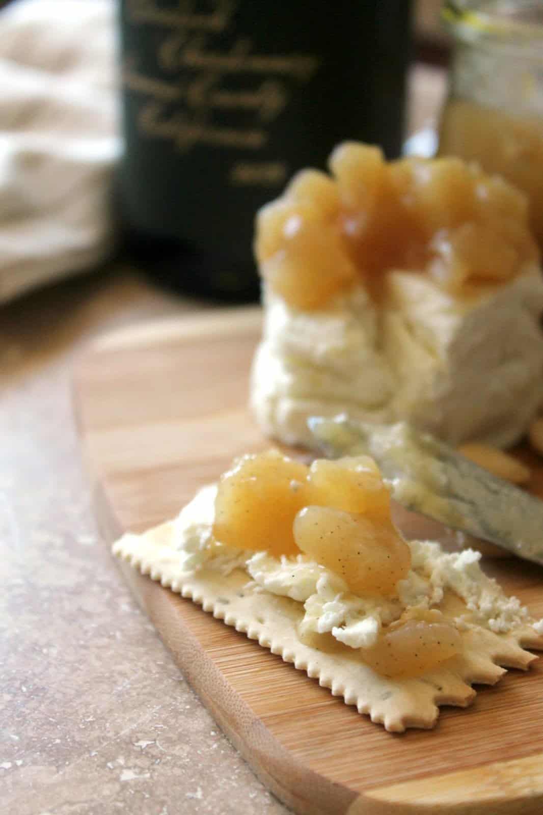 A cracker on a wooden board spread with goat cheese and pear compote.