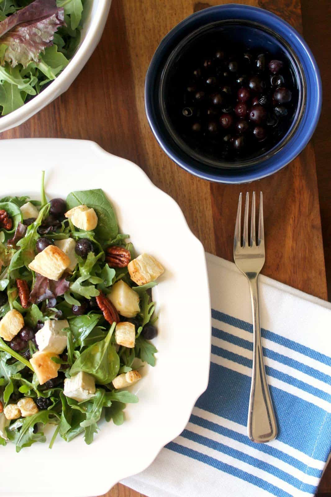 A fork next to a salad with brie, blueberries, pecans and puff pastry croutons.