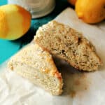 Two lemon poppy seed scones on a piece of parchment with lemons behind them.