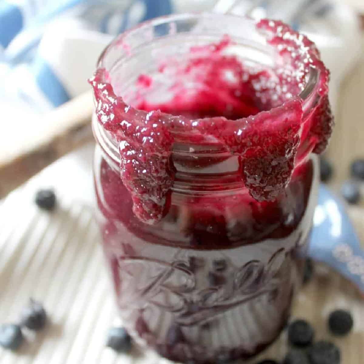 Blueberry BBQ Sauce in a mason jar with blueberries scattered beside it.