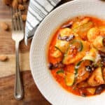 Zucchini Ribbons in Romesco Sauce in a white bowl with a fork & ingredients next to it.