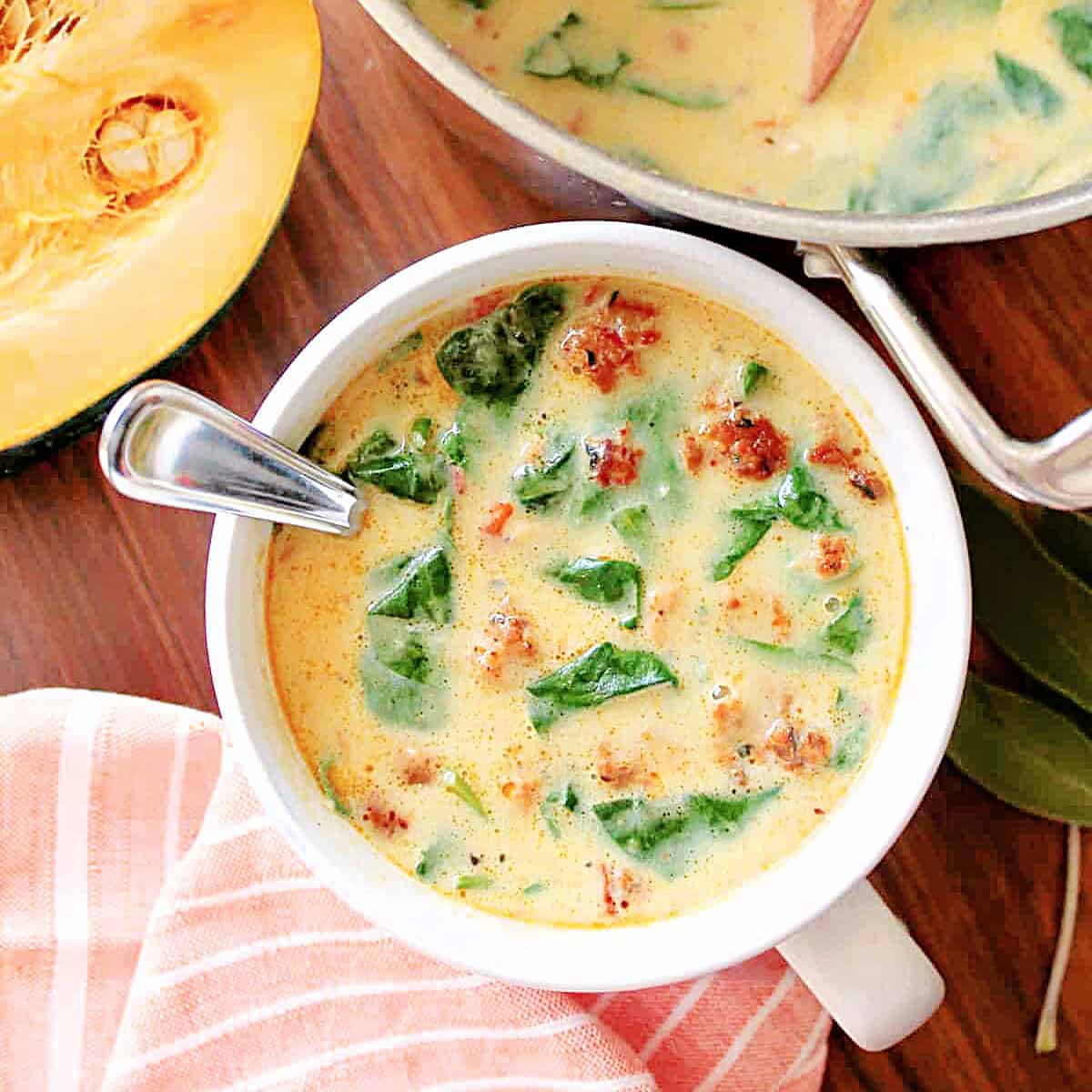 Sausage & Squash Soup in a white mug with ingredients around it.