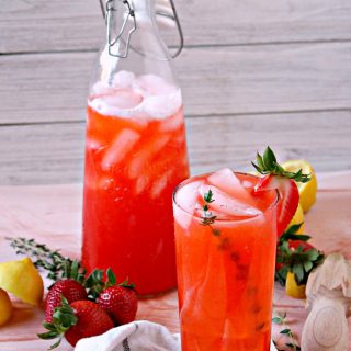 Strawberry thyme lemonade in a glass with carafe in the background.