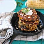 A stack of sweet corn and black bean fritters in a mini cast iron skillet with fresh sweet corn in the background.