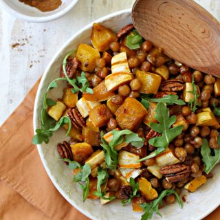 Pumpkin-Spiced Roasted Squash & Chickpea Salad! Need something a little different to serve alongside your holiday staples? This warm salad dish is sweet, savory and filled with the flavors and aromas of the holiday season!  Delicata squash is having a moment. I noticed its popularity on the rise last fall, and I've continued to see more and more people using it lately. I never jumped on the bandwagon last year, but when I started seeing them piled into pretty mounds at Trader Joe's at the start of autumn this year, I figured it couldn't hurt to toss a few in my cart and experiment with them at home. Now that I've cooked with them several times, I don't know why it took me so long to get on board! If you like squash but dread dealing with prepping it, then Delicata is the perfect variety for you. Unlike its tough-skinned counterparts, there is no need to peel Delicata squash which makes it a huge time saver. Since it's typically smaller than butternut squash and not quite as wide as an acorn squash, it's also much easier to chop, which I deeply appreciate since I can't tell you how many times I've feared for my digits. {This is also the reason butternut squash is one of the only vegetables I buy pre-chopped -- unharmed fingers are totally worth the convenience charge, if you ask me.} Anyway, I bought some Delicata squash a few weeks ago to serve as a side dish when I had my family over for dinner, and everyone raved about how I prepared it so much that I decided I'd work on a Thanksgiving-worthy recipe to share here using the gourd-du-jour. This Pumpkin-Spiced Delicata Squash & Chickpea Salad is what I came up with! I know I throw this phrase around a lot, but it is SO EASY to make, especially since that Delicata squash is so much less difficult than the other kinds. You just chop, drop and toss everything with a mixture of oil, maple syrup and seasoning {salt and pumpkin spice blend to be exact} on one sheet pan, and let the oven do the rest of the work. The maple syrup glazes both the squash and the chickpeas, caramelizing everything as it roasts, and makes them taste like candy. The pumpkin spice pairs like a a dream with the naturally sweet and creamy interior of the squash. Ugh. It's so good. If you want to simplify the prepping even further, you don't need to chop the squash into cubes if you don't want to -- it's fairly quick-cooking even when it's sliced in larger pieces. I thought the cubes worked well with the size of the chickpeas to make it easily "poppable", but you can chop it however you'd like. Finish it off by tossing in some pecans or pumpkin seeds, and maybe a handful of chopped greens for color and freshness, and you've got a new side dish for you Thanksgiving table that will be joining Delicata squash in the highest rankings of supermarket superlatives, taking the "Most Requested Side Dish" category every year. ;)