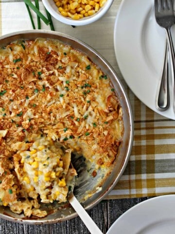 Sour Cream & Chive Corn Casserole in a skillet on a table with white plates. 