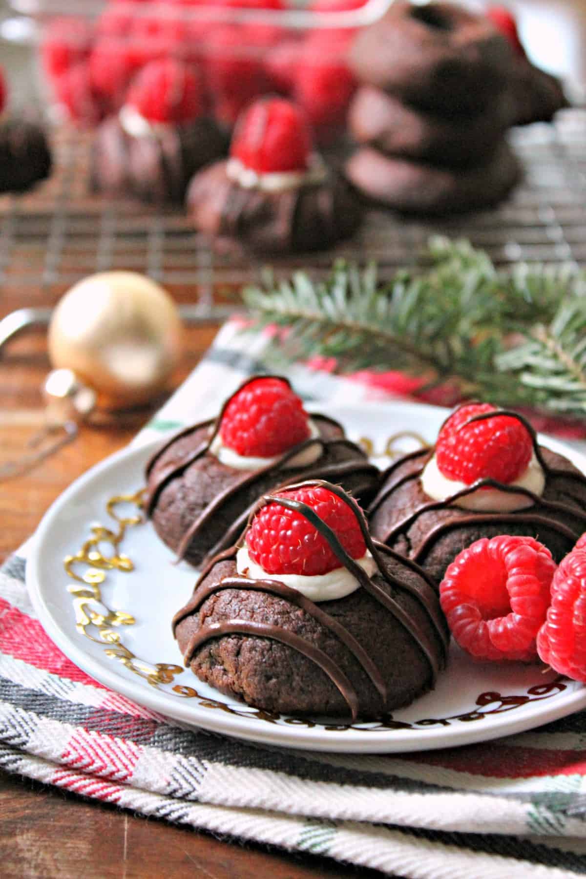 Raspberry Cheesecake Chocolate Thumbprint Cookies! This thumbprint cookie recipe will become a family favorite: Tender chocolate cookies filled with creamy "cheesecake" filling, fresh raspberries and topped with a chocolate drizzle! A beauty to share for holiday cookie exchange parties and beyond.