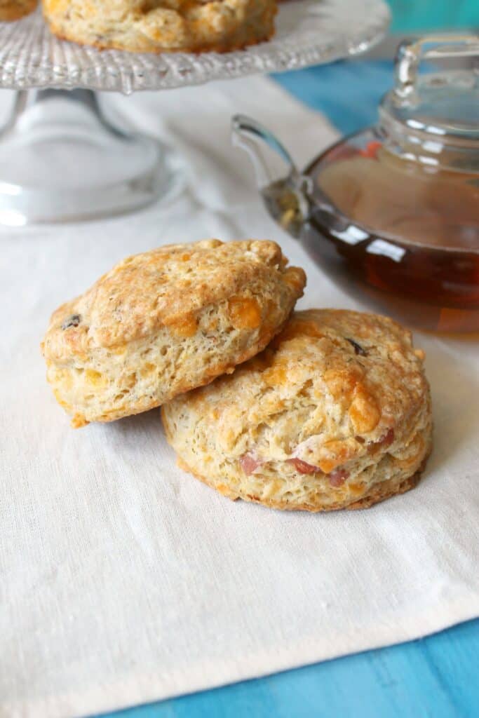 Two ham and cheese scones on a cloth napkin with a clear teapot in the background.