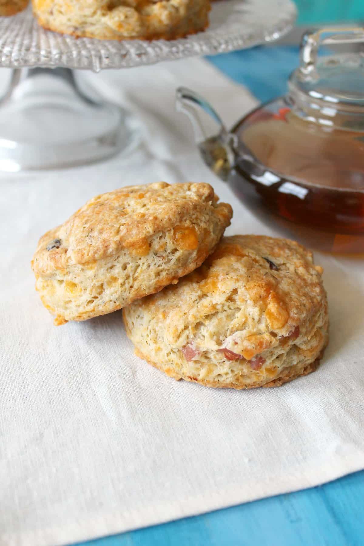 Two ham and cheese scones on a cloth napkin with a clear teapot in the background.