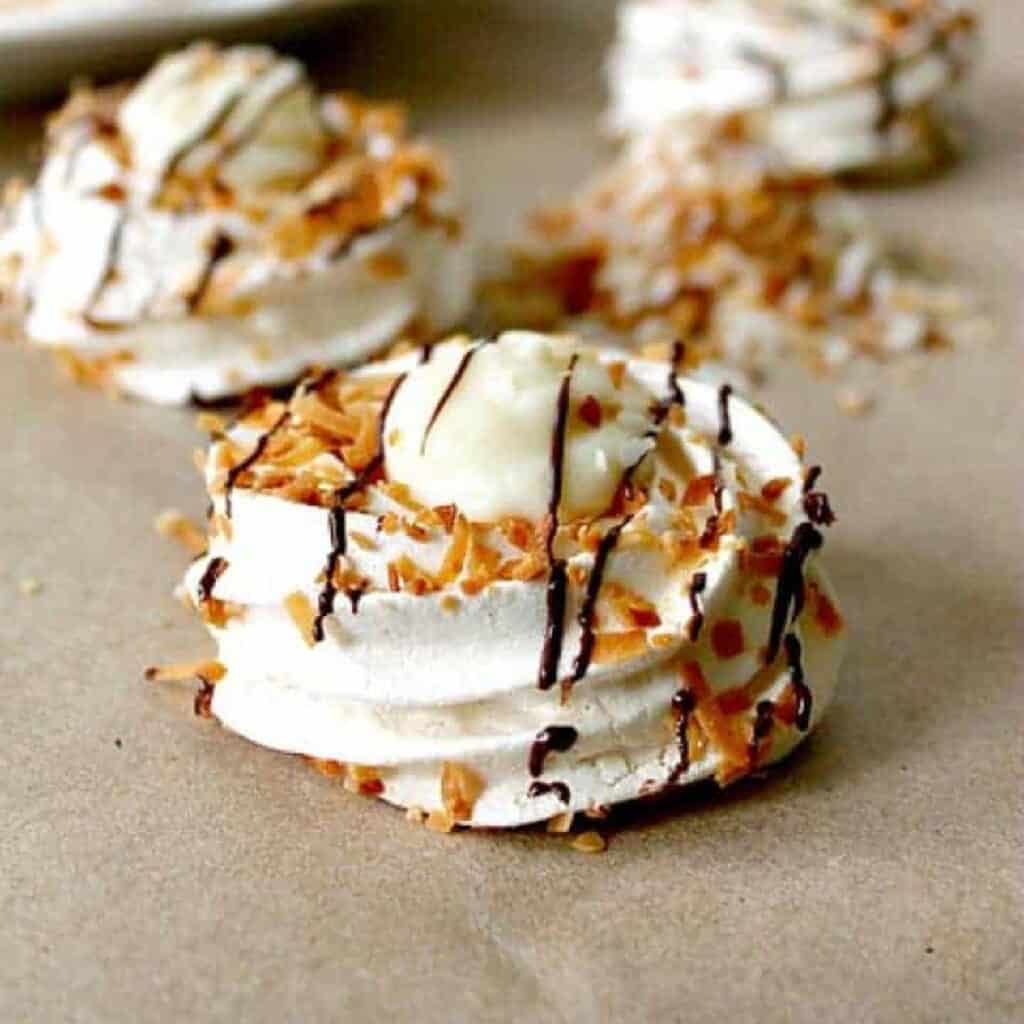 A pavlova nest with coconut custard filling sprinkled with coconut flakes and drizzled with chocolate.