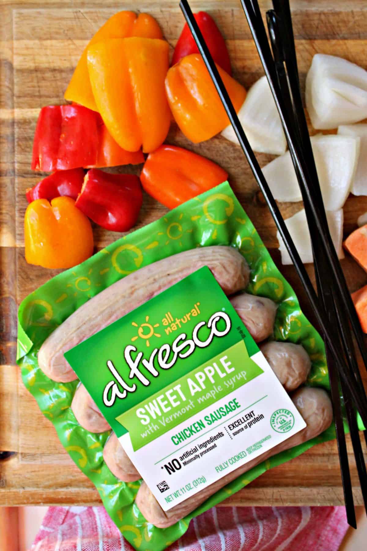 Close up of al fresco chicken sausage packaging with cut up vegetables and kabob skewers.