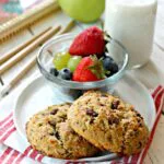 Two breakfast cookies on a small plate with a bowl of fruit on the side.