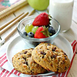 Two breakfast cookies on a small plate with a bowl of fruit on the side.