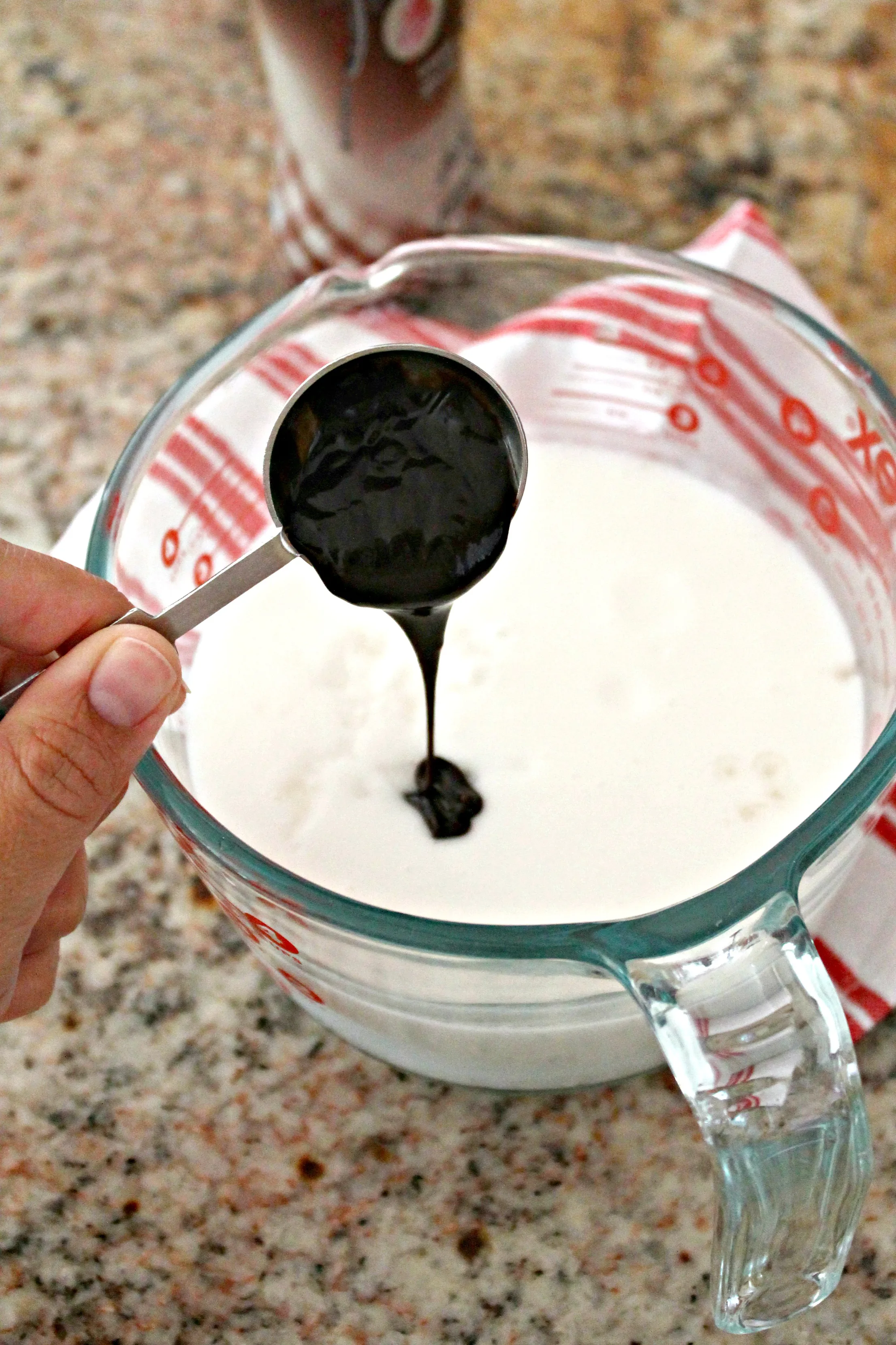 Preparation shot of chocolate syrup being added to a measuring cup of milk.