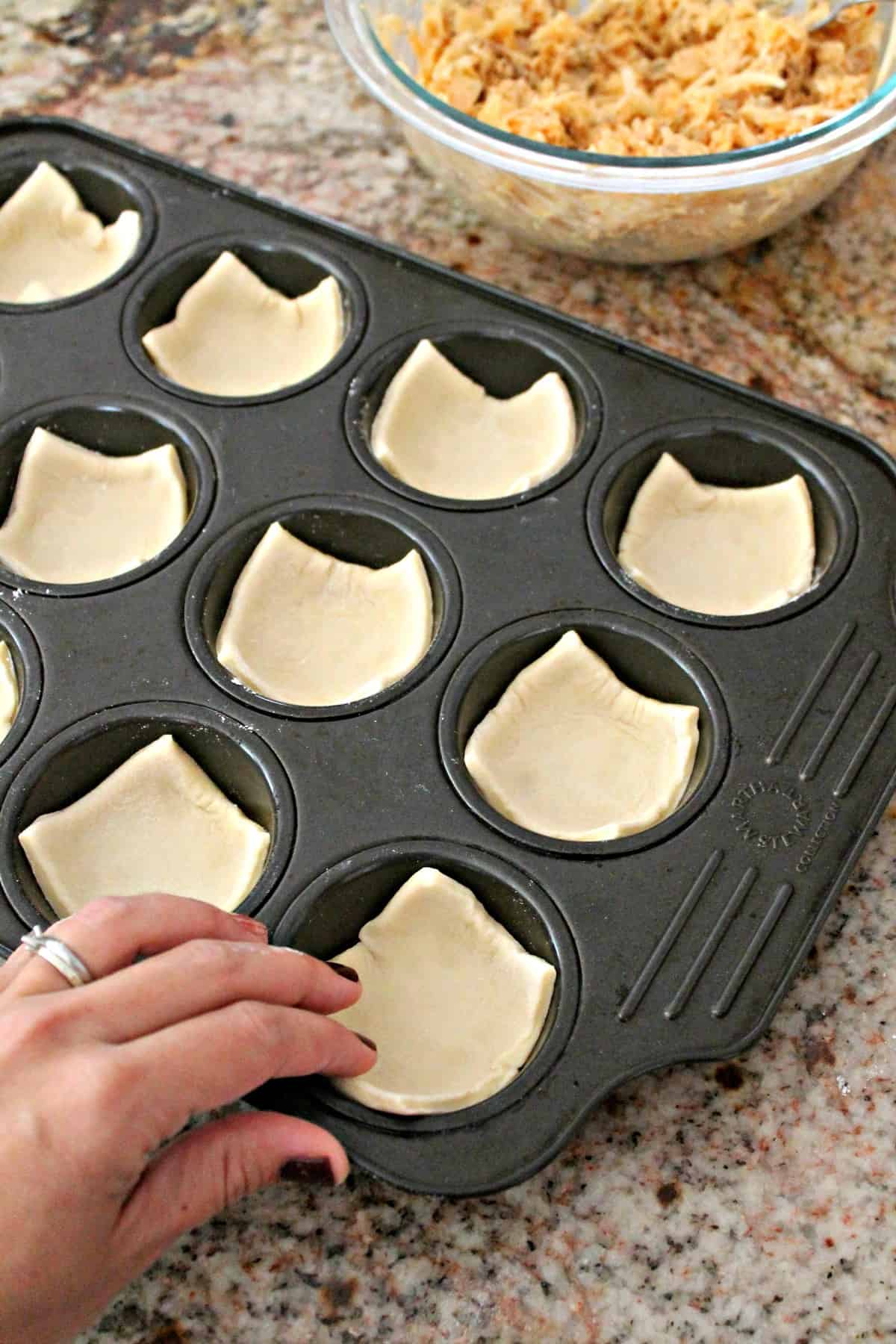 Process shot: Placing puff squares pastry in muffin tins.