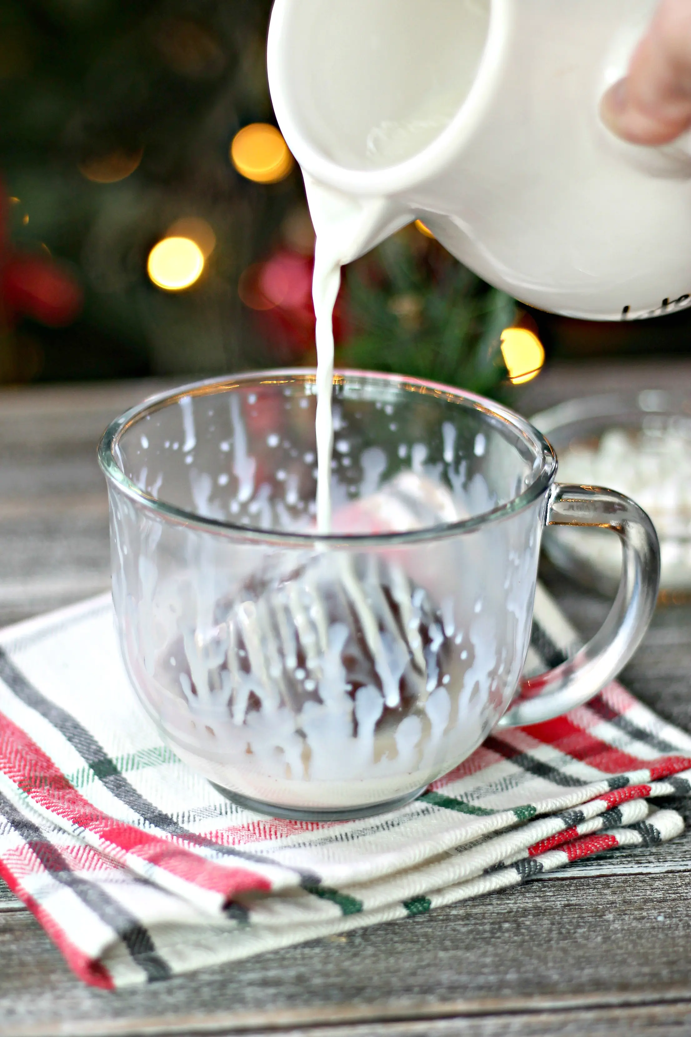 Hot milk being poured over a hot chocolate bomb in a clear mug.