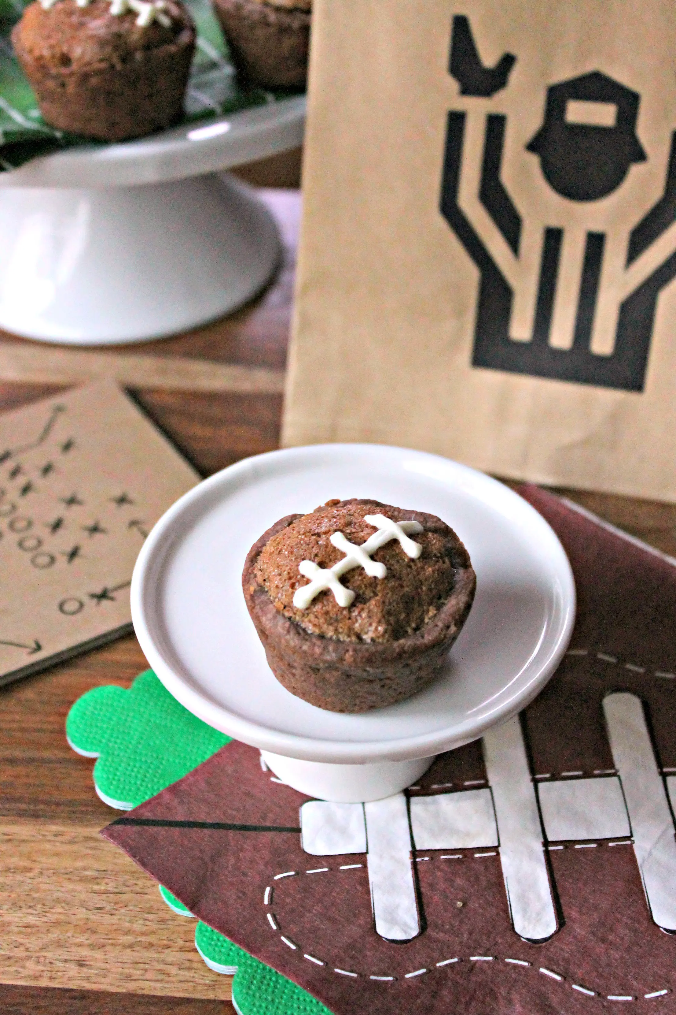 Image of a Football Pie Cookie Cup on a mini white cake plate surrounded by football party supplies.