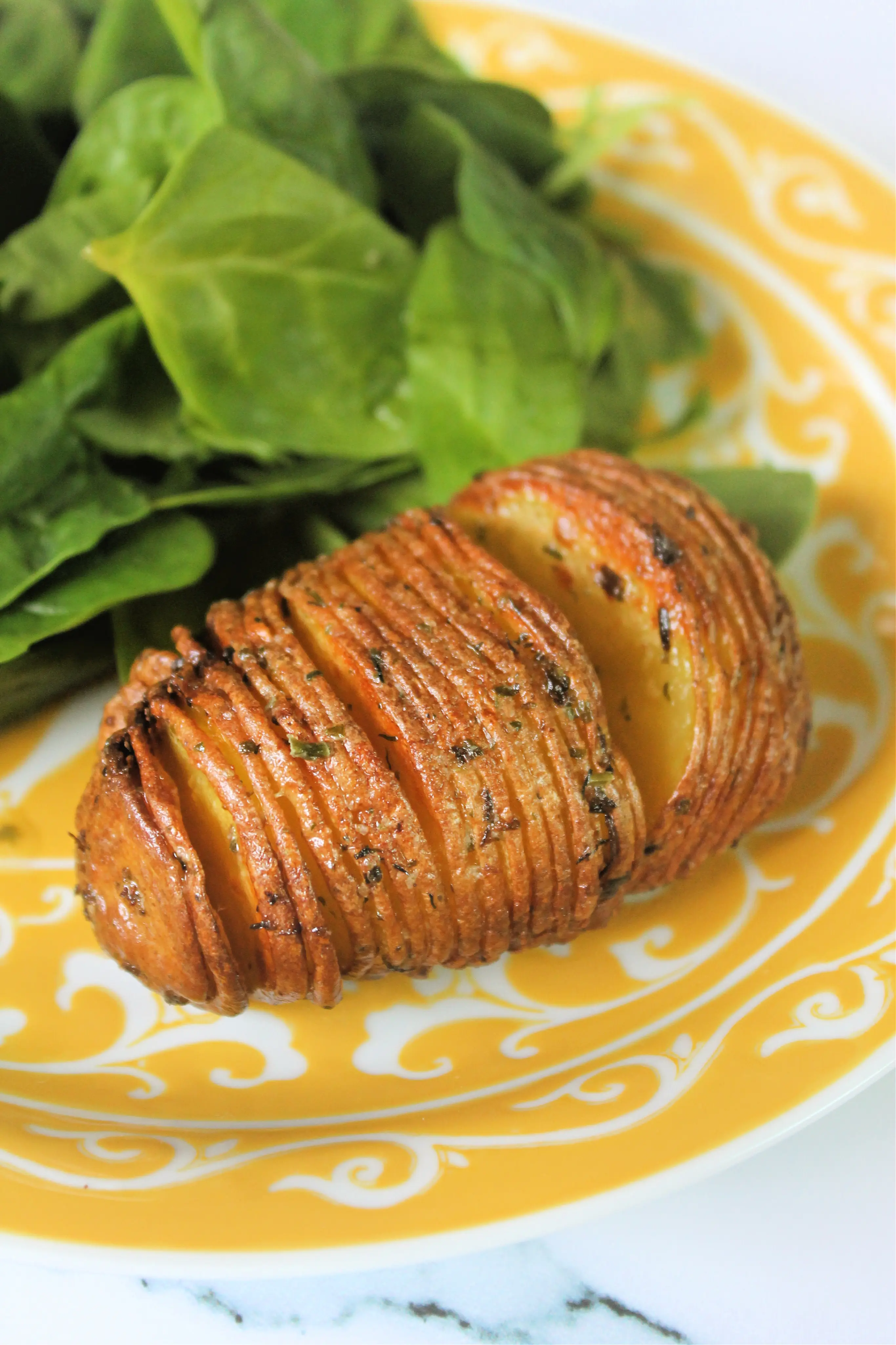 Close up of hasselback potato on yellow plate.