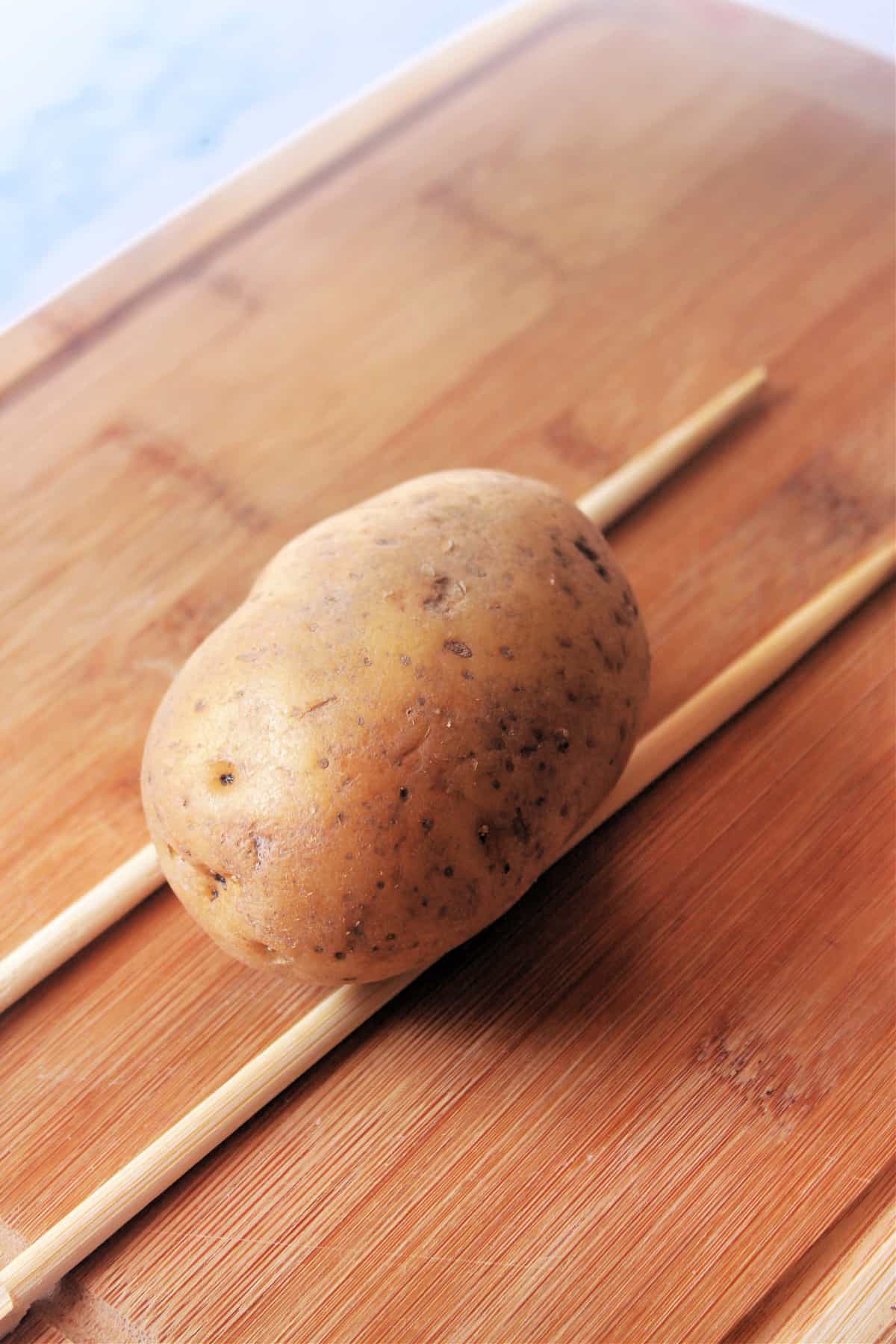 Process shot of potato on cutting board with chopsticks on either side.