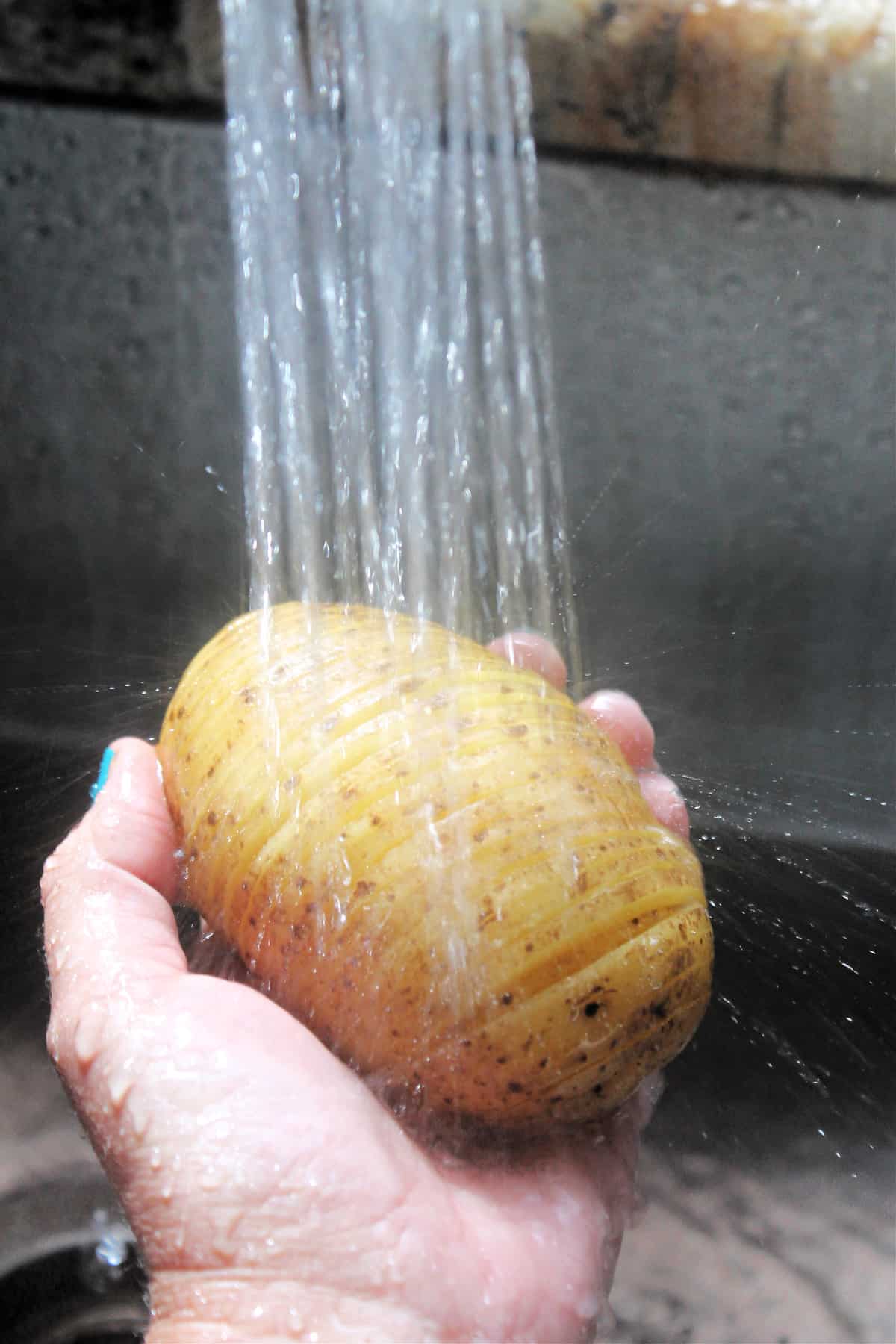 Process shot of rinsing potato under cold water.