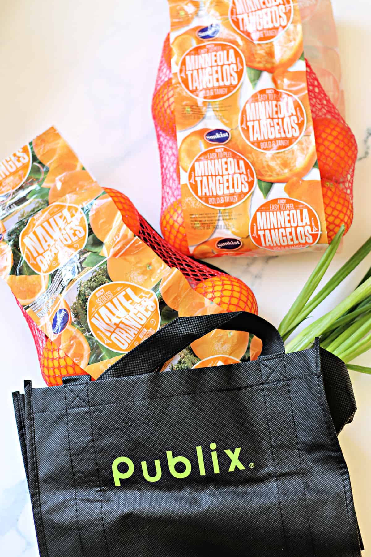 Overhead shot of Publix bag on a countertop with two bags of oranges and green onions coming out of bag.
