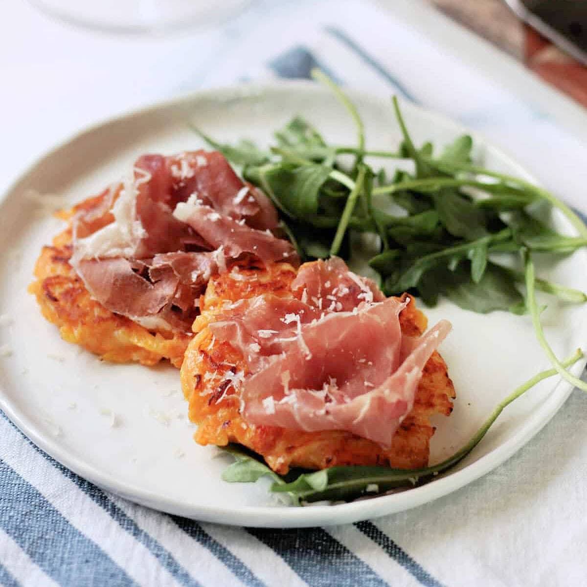 Butternut Squash Fritters topped with prosciutto on a white appetizer plate.